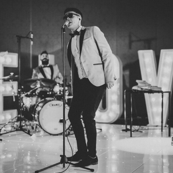 Wedding live band performing on stage with singer and musicians in formal attire, entertaining guests at a reception with illuminated ‘LOVE’ letters.