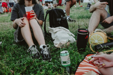People sitting on grass at an outdoor festival enjoying drinks and food during a casual daytime gathering in Singapore