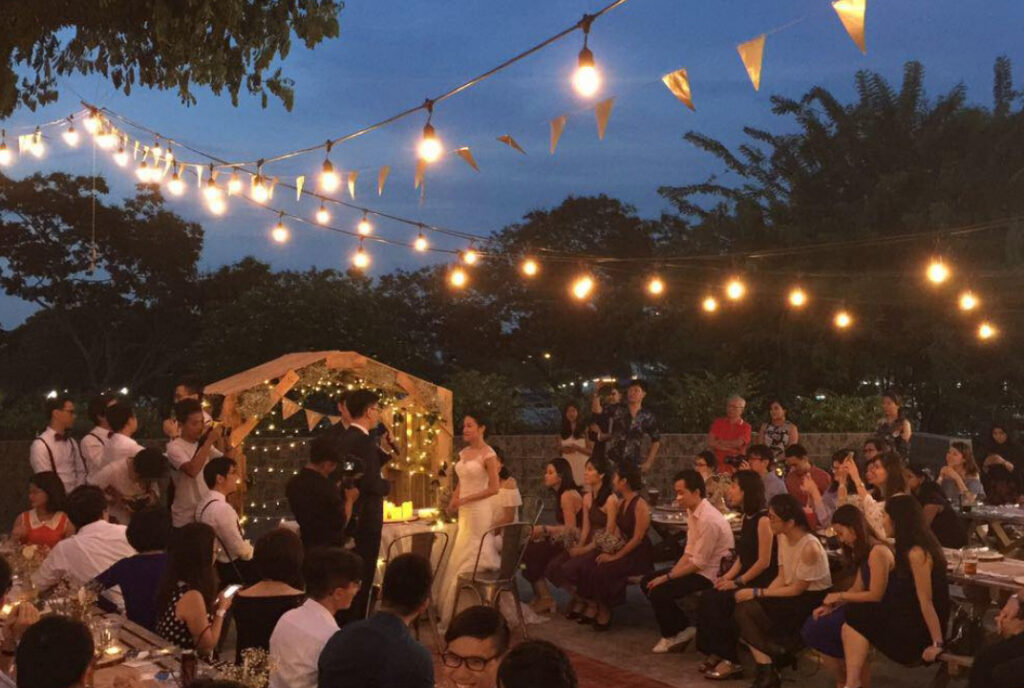 An outdoor evening wedding reception at Little Island Brewing Co, Changi Village, with string lights and fairy-lit arch