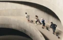 Four runners ascend a curved concrete ramp in a multi-storey car park, captured mid-stride from above during an On Squad Race event.