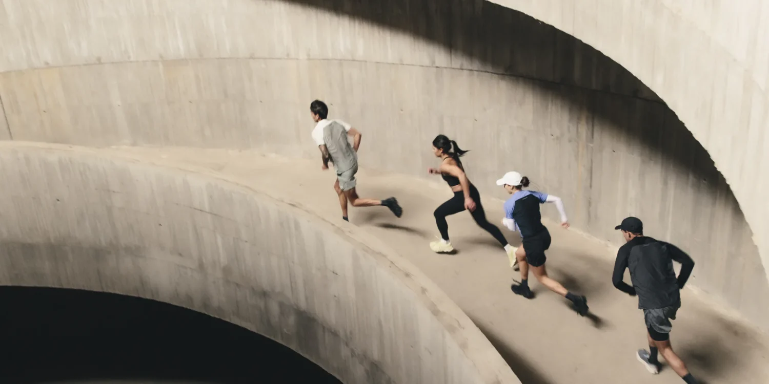 Four runners ascend a curved concrete ramp in a multi-storey car park, captured mid-stride from above during an On Squad Race event.