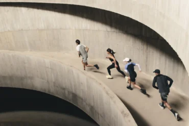 Four runners ascend a curved concrete ramp in a multi-storey car park, captured mid-stride from above during an On Squad Race event.