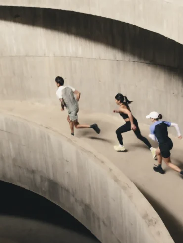 Four runners ascend a curved concrete ramp in a multi-storey car park, captured mid-stride from above during an On Squad Race event.