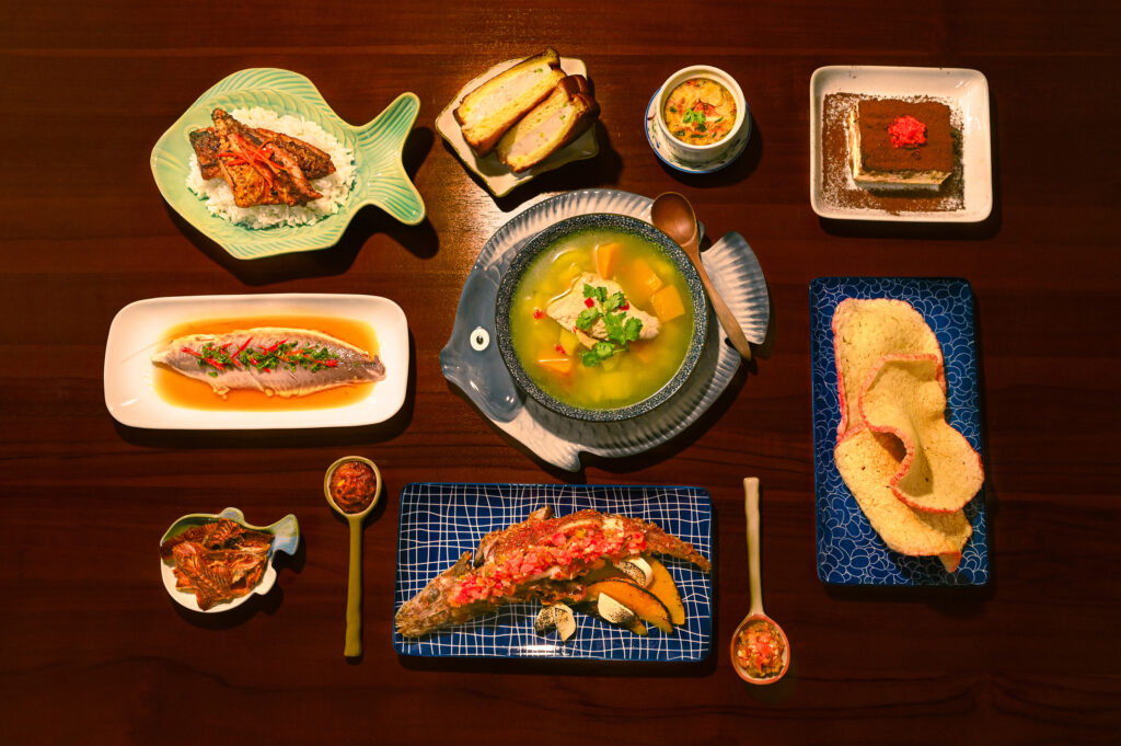 A spread of dishes from Pasarfish at Chef X, including steamed fish, fish-shaped plates of soup and rice, a tiramisu-style dessert topped with tobiko, crispy fish crackers, and a whole grilled fish head with salsa.