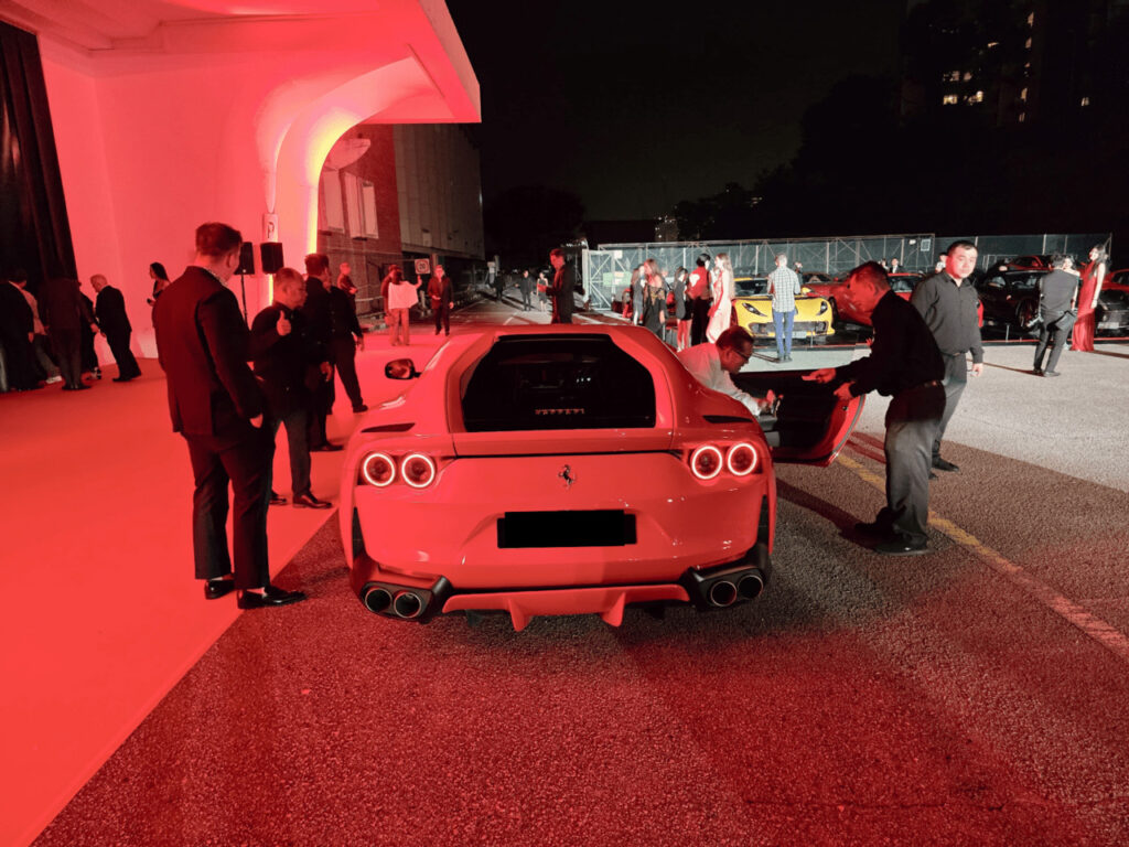 A valet attendant attending to a red Ferrari at a formal evening event in Singapore