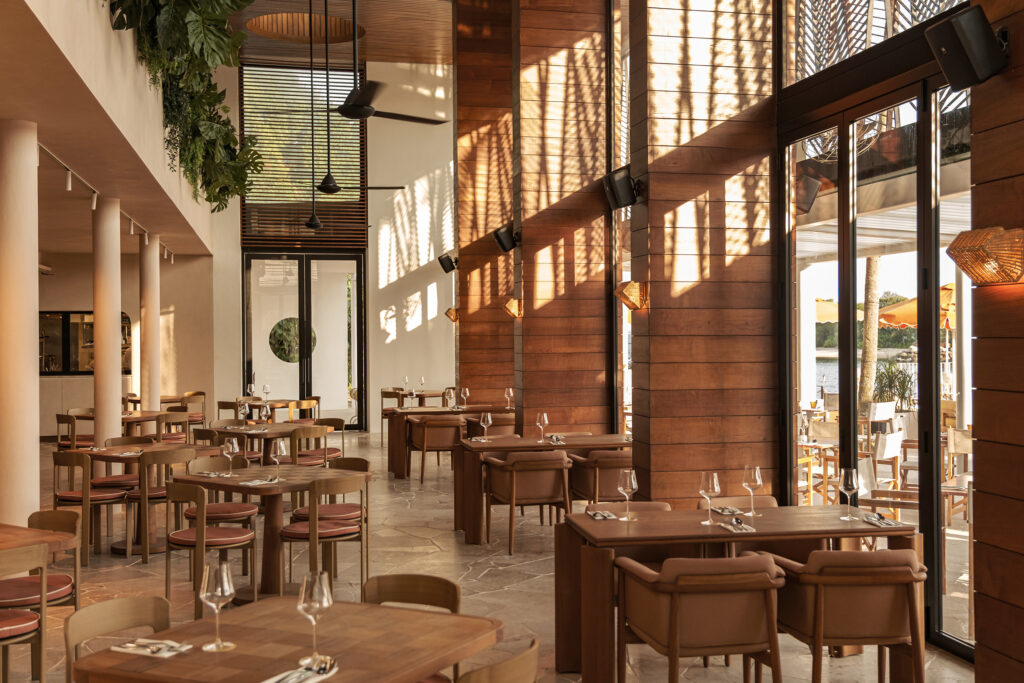 The warm, sun-lit interior of Tanjong Beach Club with wooden furnishings and views of the waterfront
