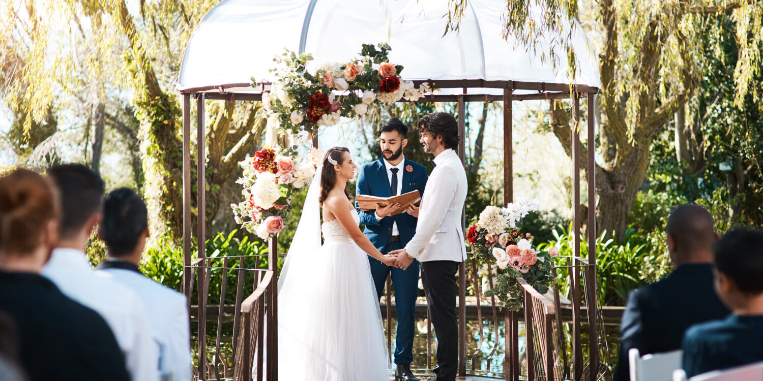 A couple exchanging vows at an outdoor garden wedding ceremony beneath a flower-adorned gazebo