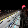 F1 cars lined up on the starting grid at the Singapore Grand Prix night race, with packed grandstands and glowing lanterns overhead.