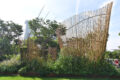 A show garden installation at Singapore Garden Festival featuring curved bamboo screens rising above a dense bed of tropical plants, with Marina Bay Sands visible in the background.