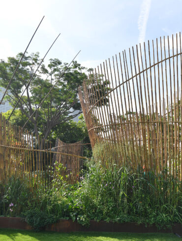 A show garden installation at Singapore Garden Festival featuring curved bamboo screens rising above a dense bed of tropical plants, with Marina Bay Sands visible in the background.