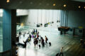 A group of travellers with luggage walks across the polished floor of a Changi Airport terminal, with directional signs to Terminal 3 and the Skytrain visible in the foreground.