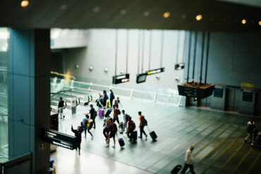 A group of travellers with luggage walks across the polished floor of a Changi Airport terminal, with directional signs to Terminal 3 and the Skytrain visible in the foreground.
