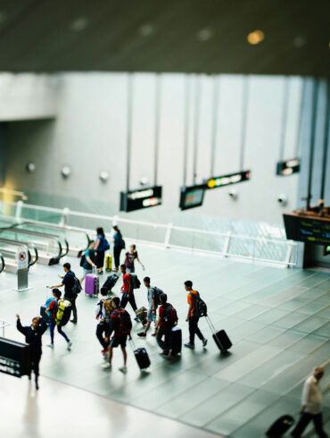A group of travellers with luggage walks across the polished floor of a Changi Airport terminal, with directional signs to Terminal 3 and the Skytrain visible in the foreground.