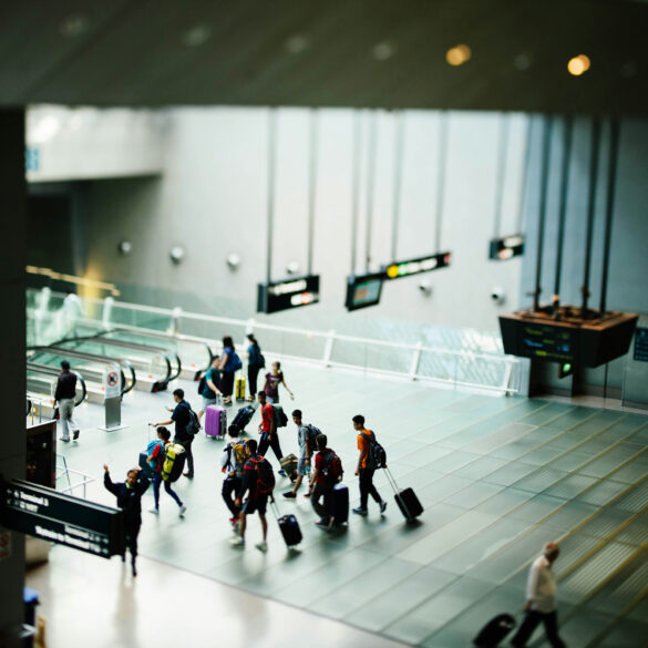 A group of travellers with luggage walks across the polished floor of a Changi Airport terminal, with directional signs to Terminal 3 and the Skytrain visible in the foreground.