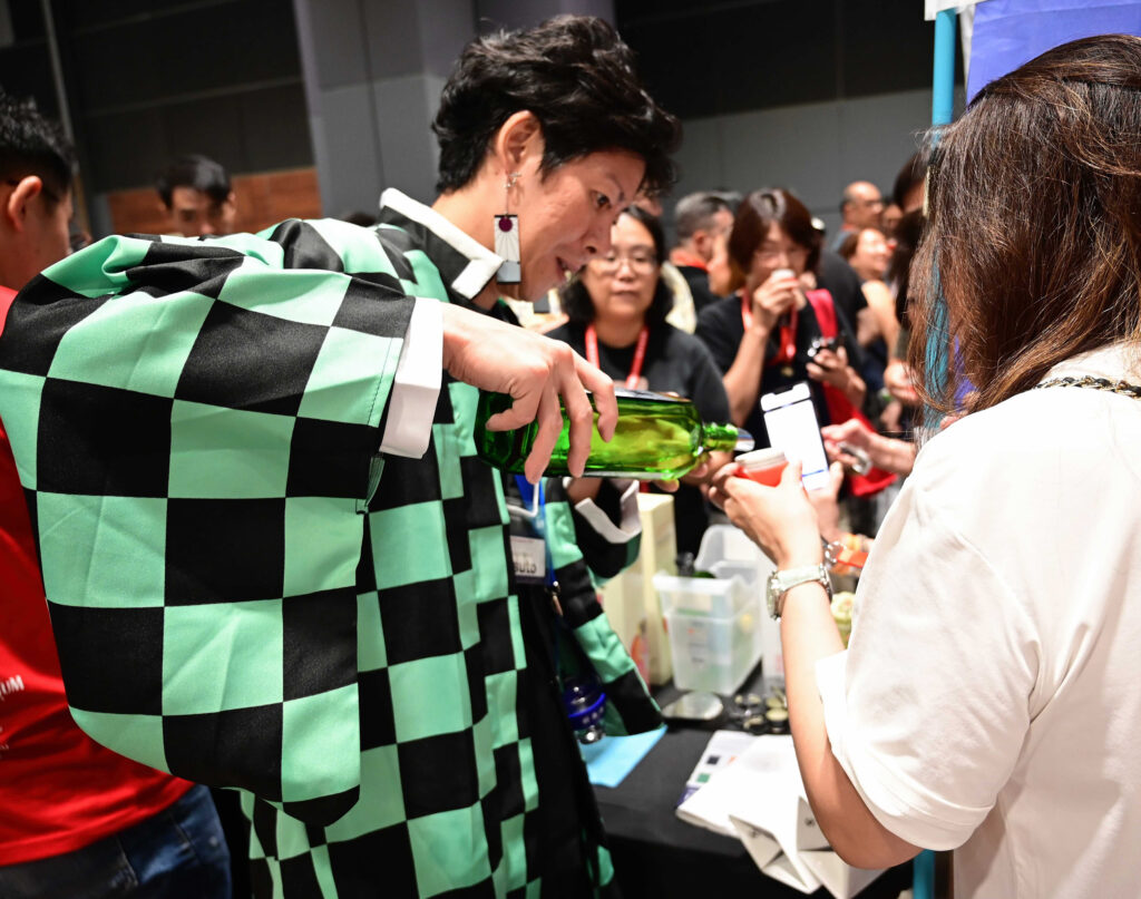 A sake brewer in a traditional Japanese haori jacket pours a sample for a visitor at Sake Festival Singapore.
