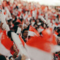 Crowd waving Singapore flags and NDP goodie bag at National Day Parade, with fluorescent light sticks lighting up the stands