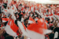 Crowd waving Singapore flags and NDP goodie bag at National Day Parade, with fluorescent light sticks lighting up the stands