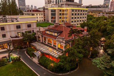 67 Pall Mall's Grand Mansion in Shanghai at dusk, with a red-tiled roof, glass conservatory and skyline backdrop.