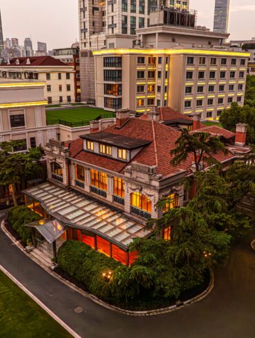 67 Pall Mall's Grand Mansion in Shanghai at dusk, with a red-tiled roof, glass conservatory and skyline backdrop.