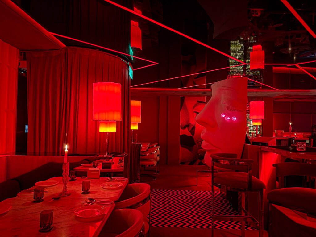 Red-lit interior of Behind Clay, with laser accents, candlelit tables and a sculptural face installation