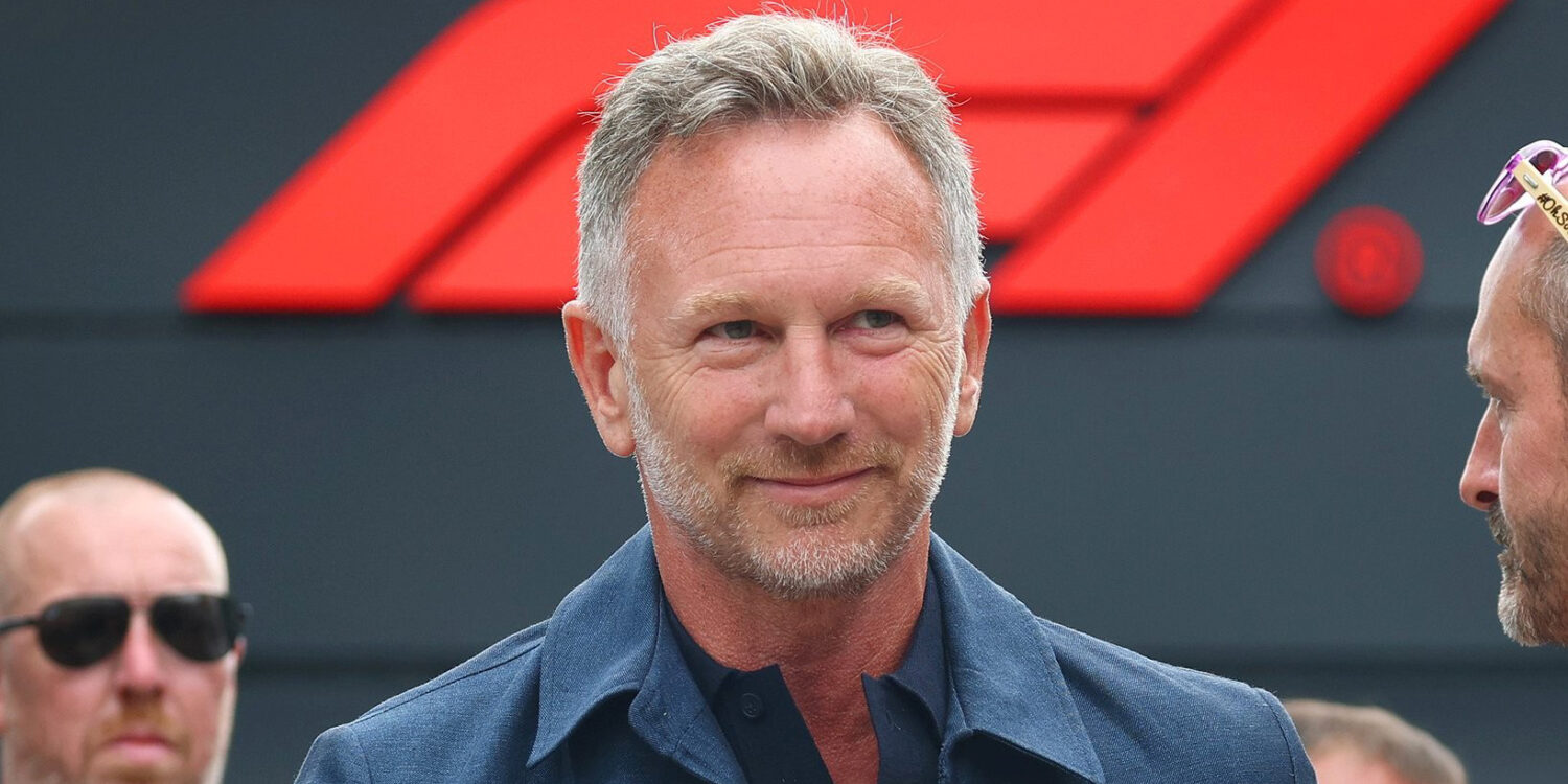 Christian Horner smiles in a navy shirt in front of an F1 logo backdrop, ahead of his Singapore live event Unfiltered