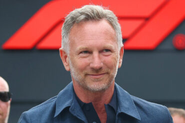 Christian Horner smiles in a navy shirt in front of an F1 logo backdrop, ahead of his Singapore live event Unfiltered