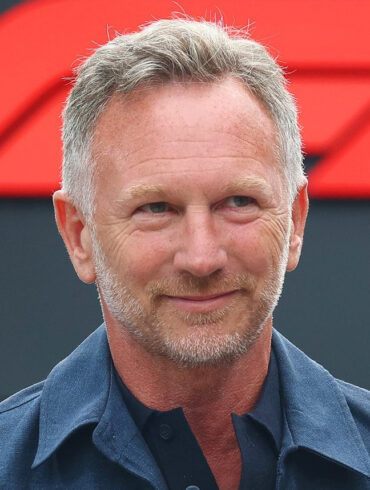 Christian Horner smiles in a navy shirt in front of an F1 logo backdrop, ahead of his Singapore live event Unfiltered