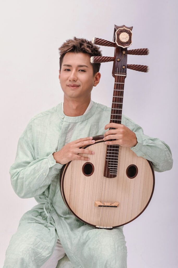 Zhongruan player Jonathan Ngeow holding his instrument, dressed in a sage green traditional-style outfit