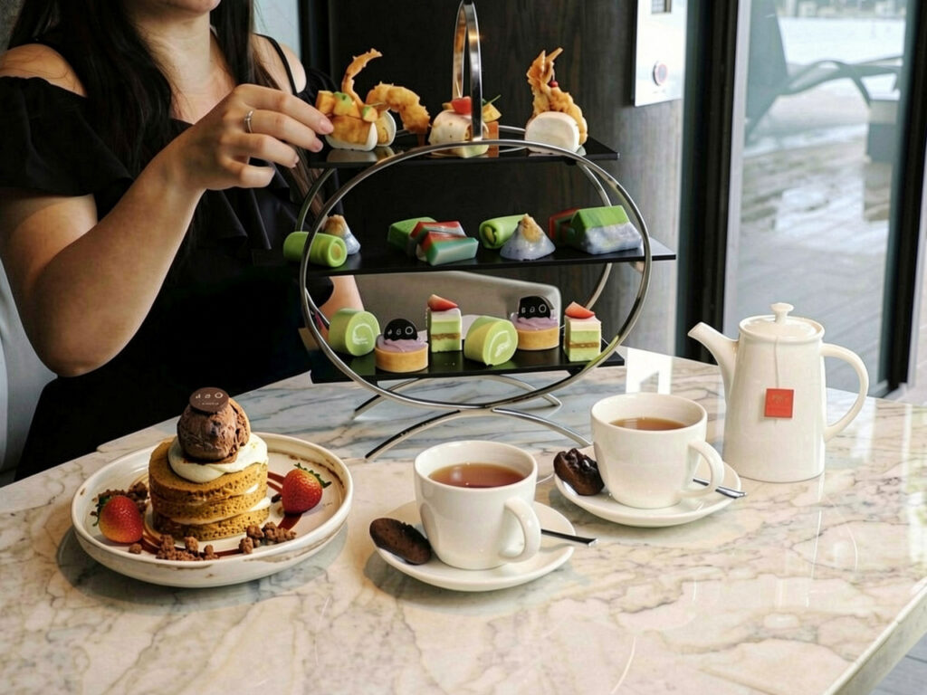 National Day Afternoon Tea spread with a three-tier stand of local-inspired bites, a matcha layer cake dessert, and pots of tea on a marble table