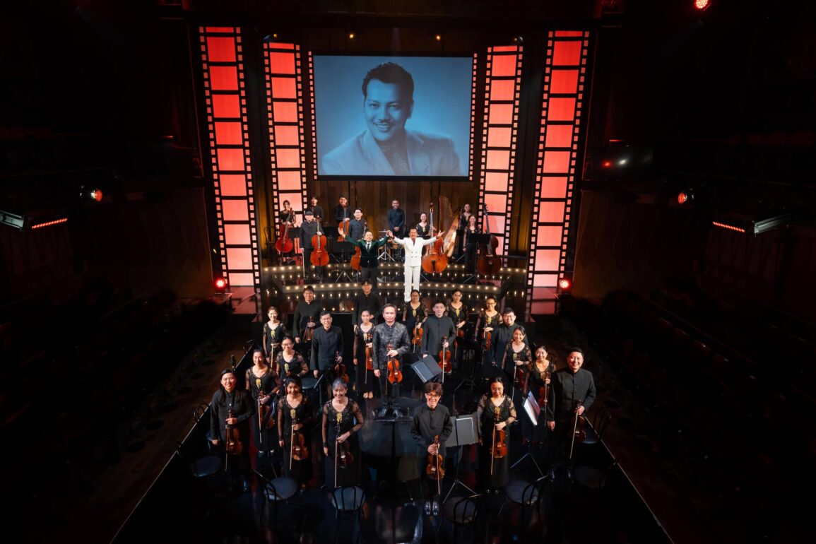 re:mix chamber orchestra and cast take a bow on stage at Wild Rice's Tunggu Sekejap: The P. Ramlee Suite, with a portrait of P. Ramlee projected behind them