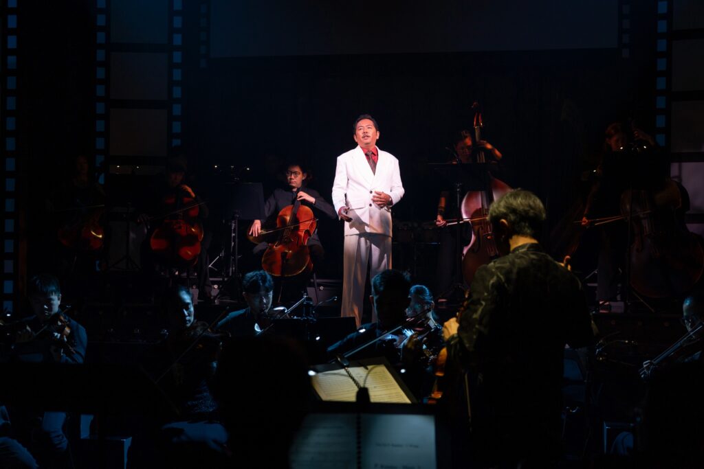 Fadhli Ramlee performs as P. Ramlee under spotlight, with conductor Foo Say Ming and re:mix orchestra strings in Tunggu Sekejap: The P. Ramlee Suite at Wild Rice