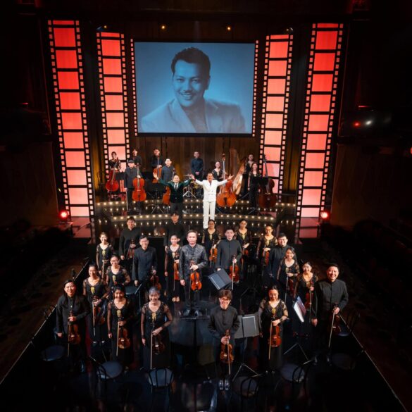 re:mix chamber orchestra and cast take a bow on stage at Wild Rice's Tunggu Sekejap: The P. Ramlee Suite, with a portrait of P. Ramlee projected behind them