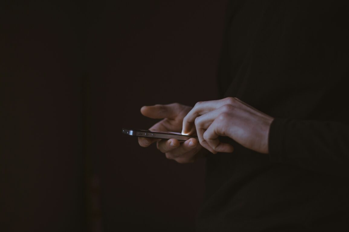 Close-up of hands typing on a smartphone in low light, representing getting in touch with City Nomads