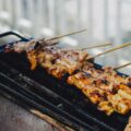 Skewers of grilled meat cooking on a charcoal grill, char marks visible on the glaze