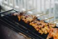 Skewers of grilled meat cooking on a charcoal grill, char marks visible on the glaze