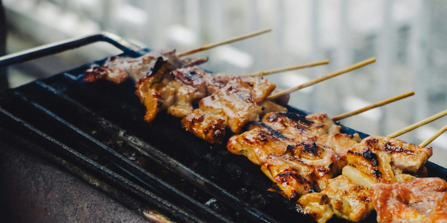 Skewers of grilled meat cooking on a charcoal grill, char marks visible on the glaze