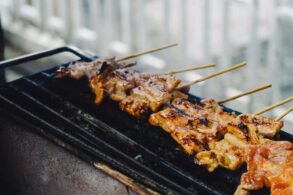 Skewers of grilled meat cooking on a charcoal grill, char marks visible on the glaze