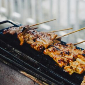Skewers of grilled meat cooking on a charcoal grill, char marks visible on the glaze