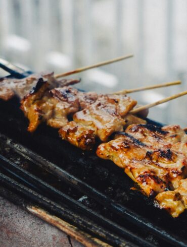 Skewers of grilled meat cooking on a charcoal grill, char marks visible on the glaze