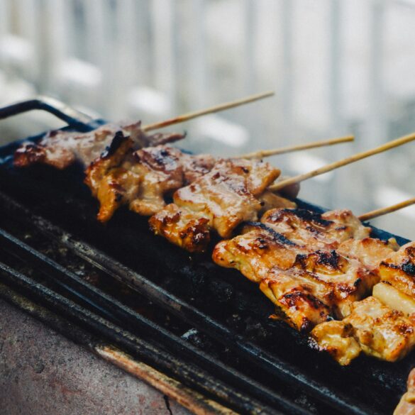 Skewers of grilled meat cooking on a charcoal grill, char marks visible on the glaze