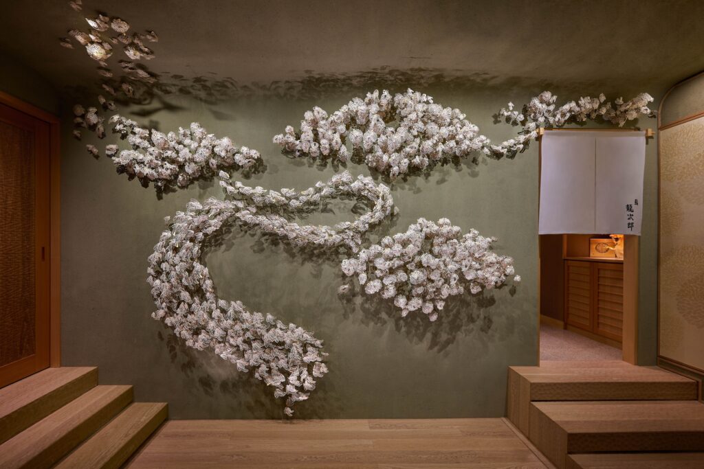 A sculptural handmade paper installation of cascading blossoms along the entrance wall of Sushi Ryujiro Singapore.