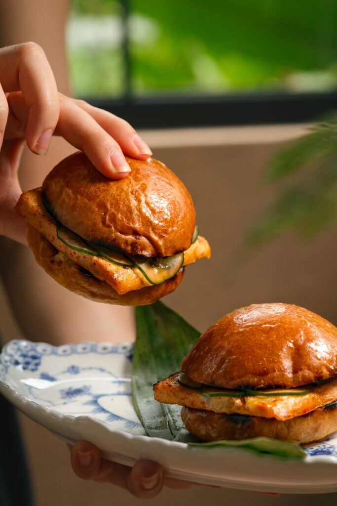 A hand holding an otak-otak slider with kaffir lime aioli on a brioche bun at Tembusu.