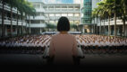 School principal in pink dress addresses uniformed students at assembly, key art for The Radicalisation of Mrs. Mary Lim-Rodrigues at Wild Rice