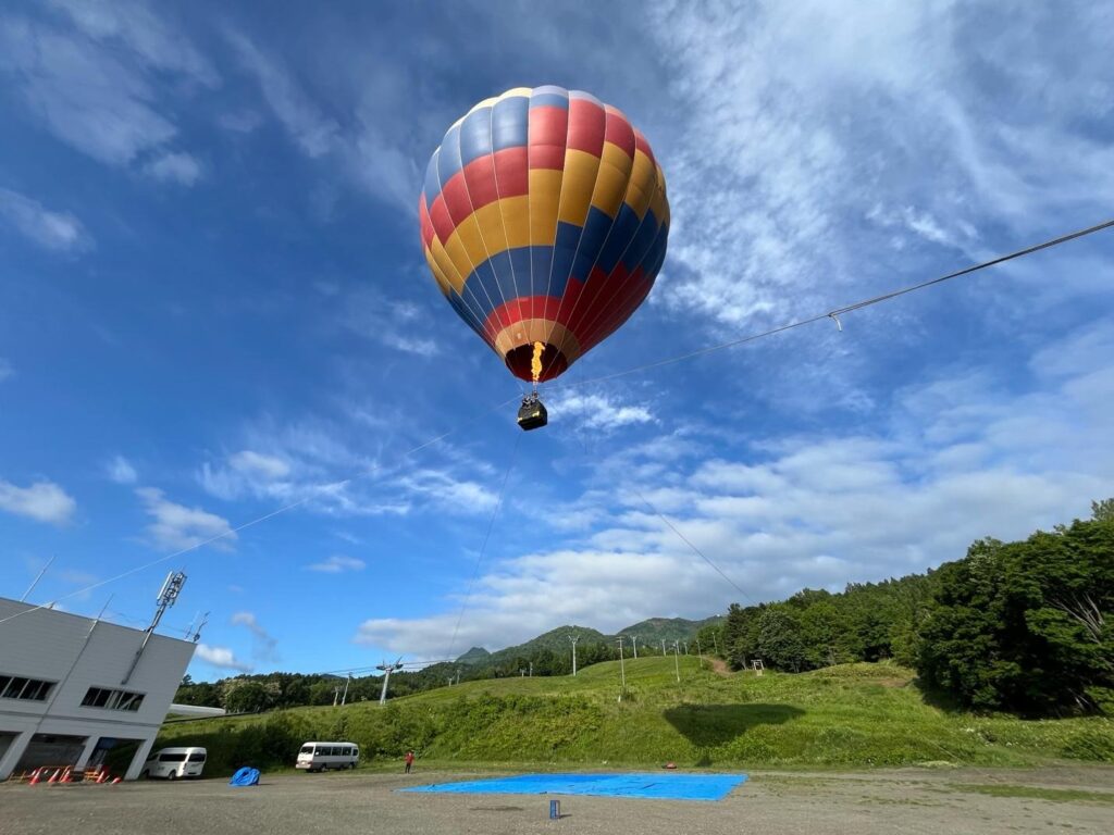Tethered hot air balloon rising over green hills near Fenix Furano in summer