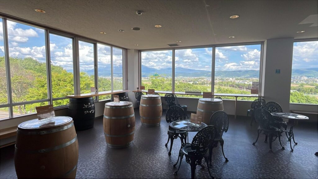 Tasting room at Furano Winery with wine barrel tables and valley views through floor-to-ceiling windows