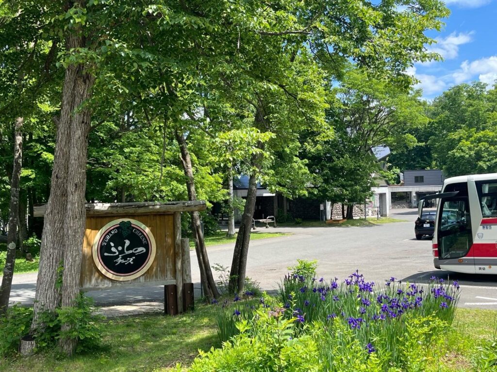 Entrance sign and parking area at Furano Cheese Factory, surrounded by trees and irises