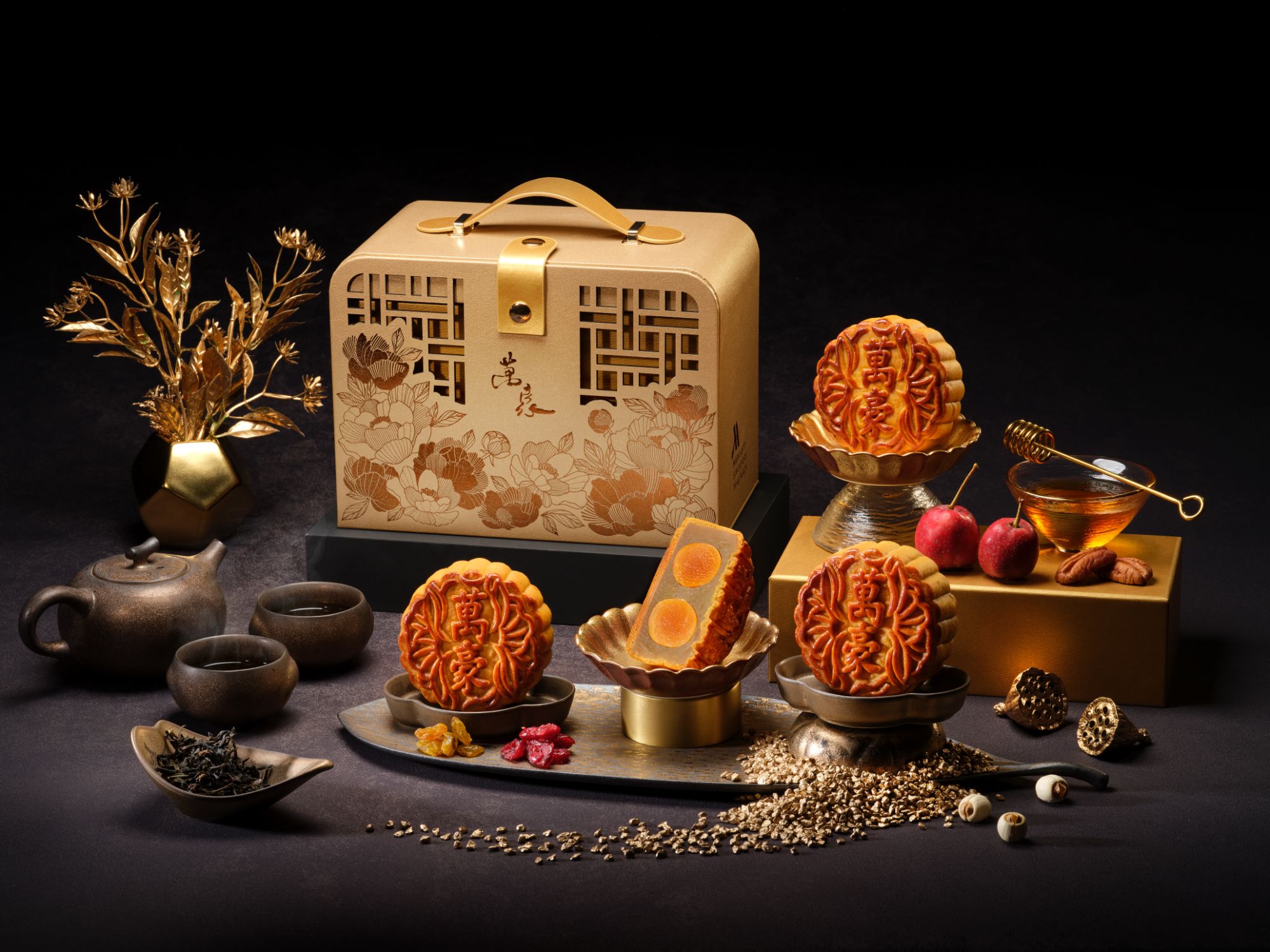 An ornate gold mooncake gift box accompanied by traditional mooncakes displayed with tea service and decorative elements.