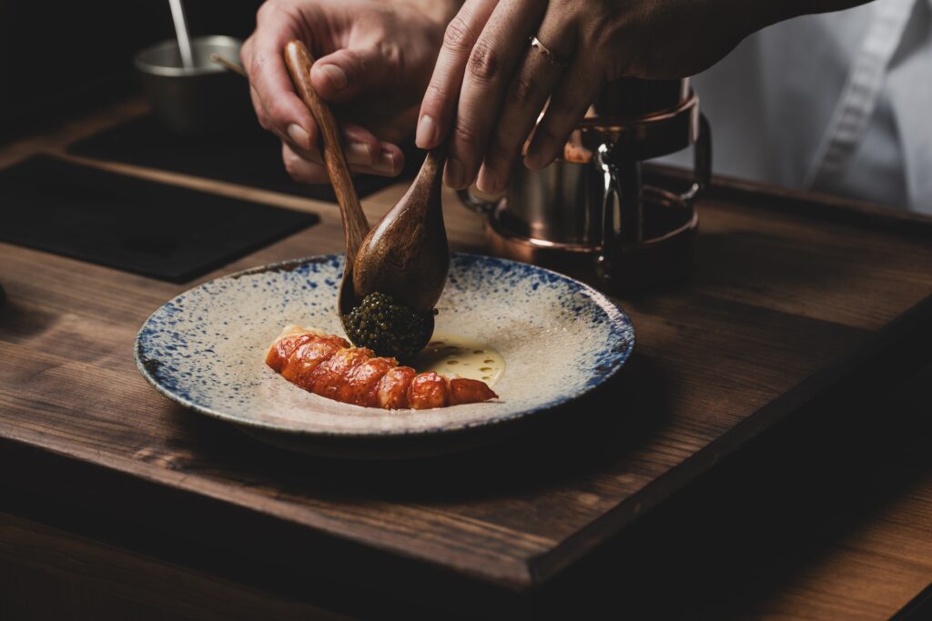 Chef's hands spooning caviar over a plated dish of marron and brown butter sauce at Zén.