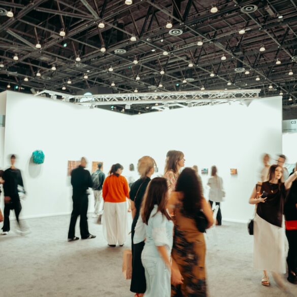 Visitors walk through a busy contemporary art fair, browsing paintings and sculptures displayed on white gallery walls