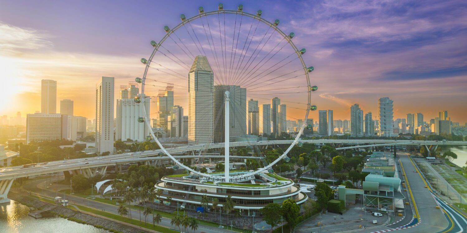 Aerial view of the Singapore Flyer and Marina Bay skyline at sunrise, with the Marina Bay Street Circuit track visible below